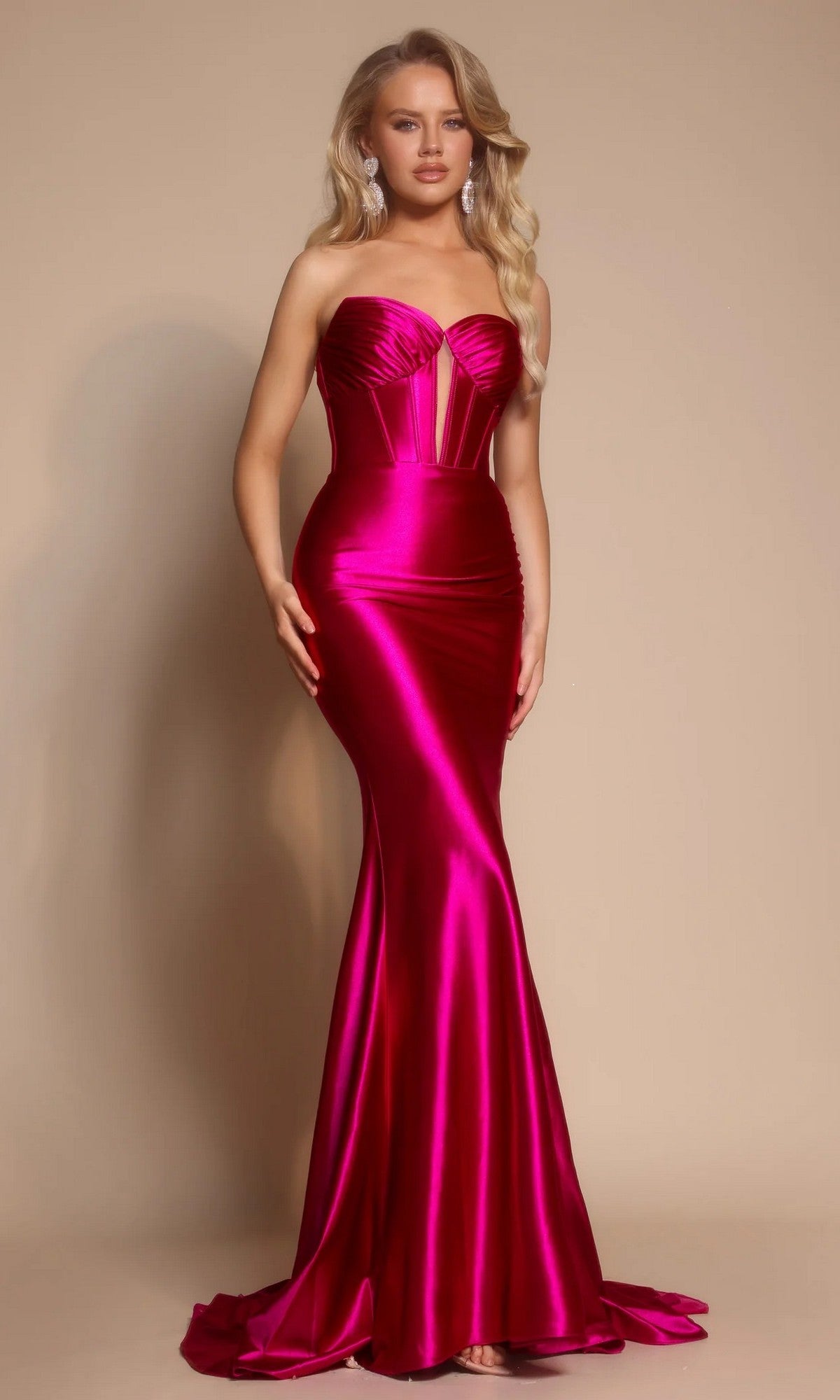 A woman poses against a beige background wearing the Portia and Scarlett XO080 long prom dress in fuchsia—a strapless, satin mermaid gown with a sweetheart neckline and form-fitting silhouette.